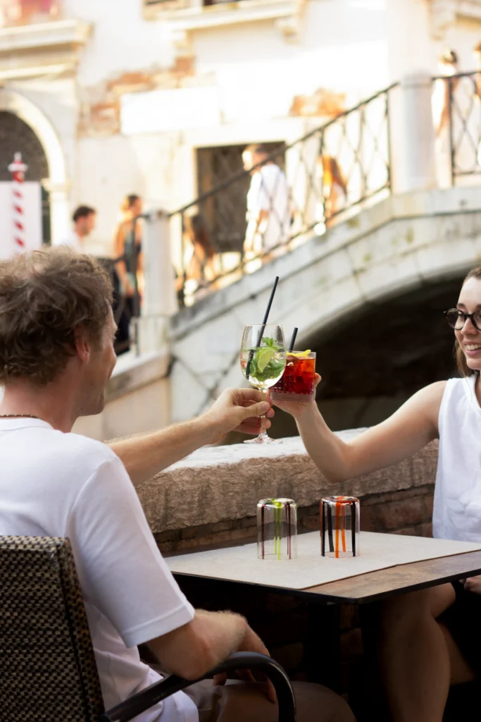 Paar stößt im Freien mit Cocktails an einem Kanal in Venedig an, Cantinone Storico